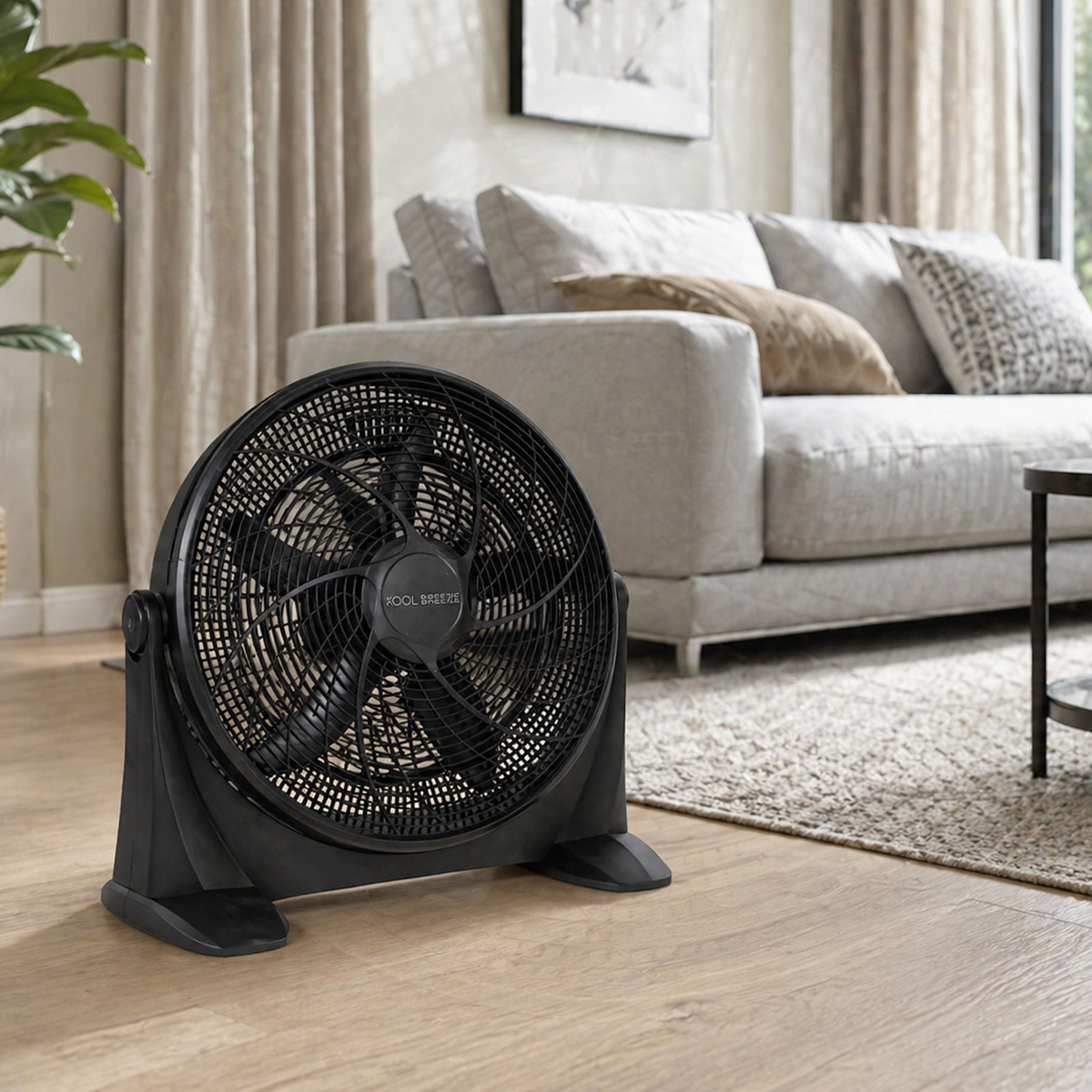 Un ventilador de suelo negro se asienta sobre un suelo de madera frente a un sofá gris y cortinas.