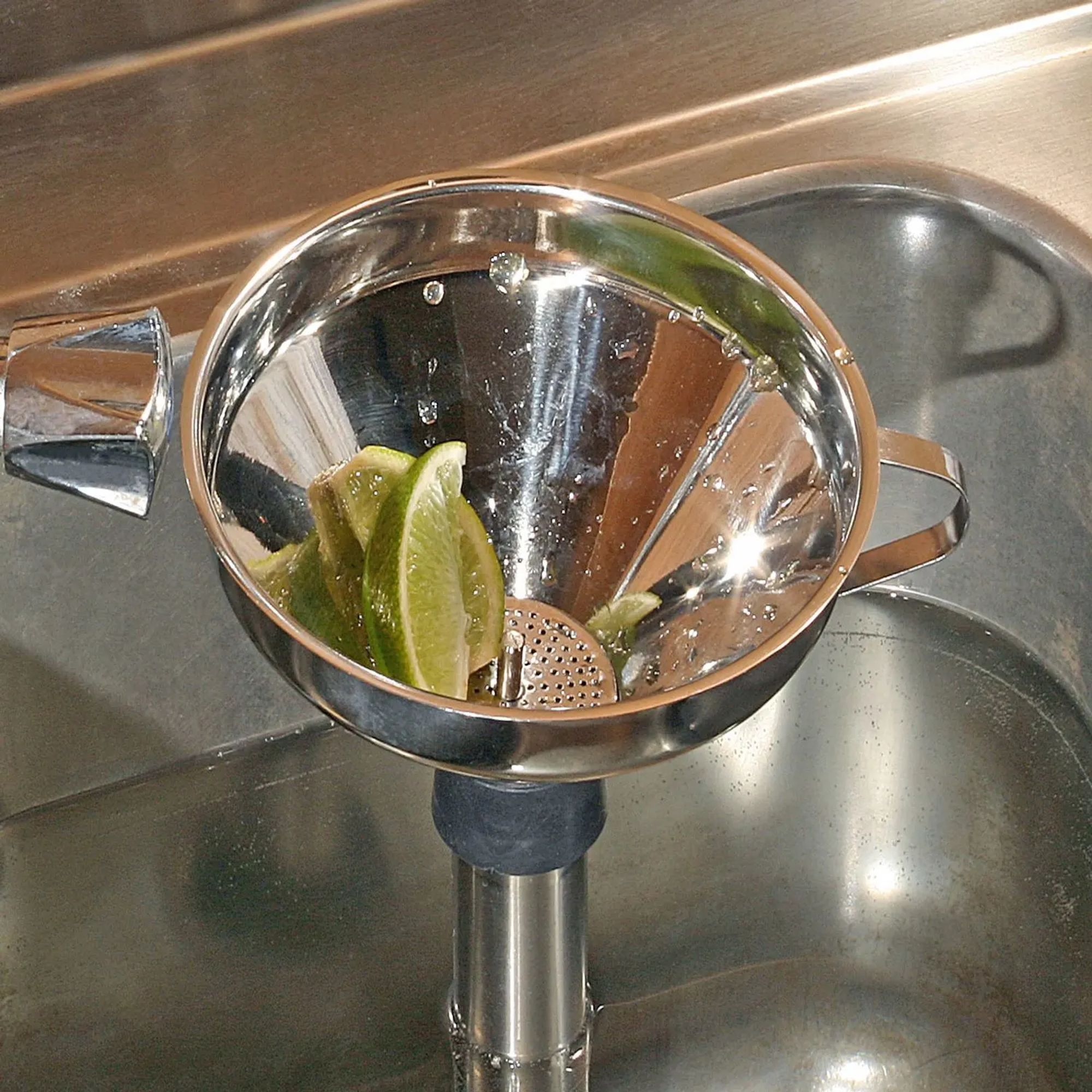 Limoenpartjes in een zilveren zeef boven een gootsteen met water.