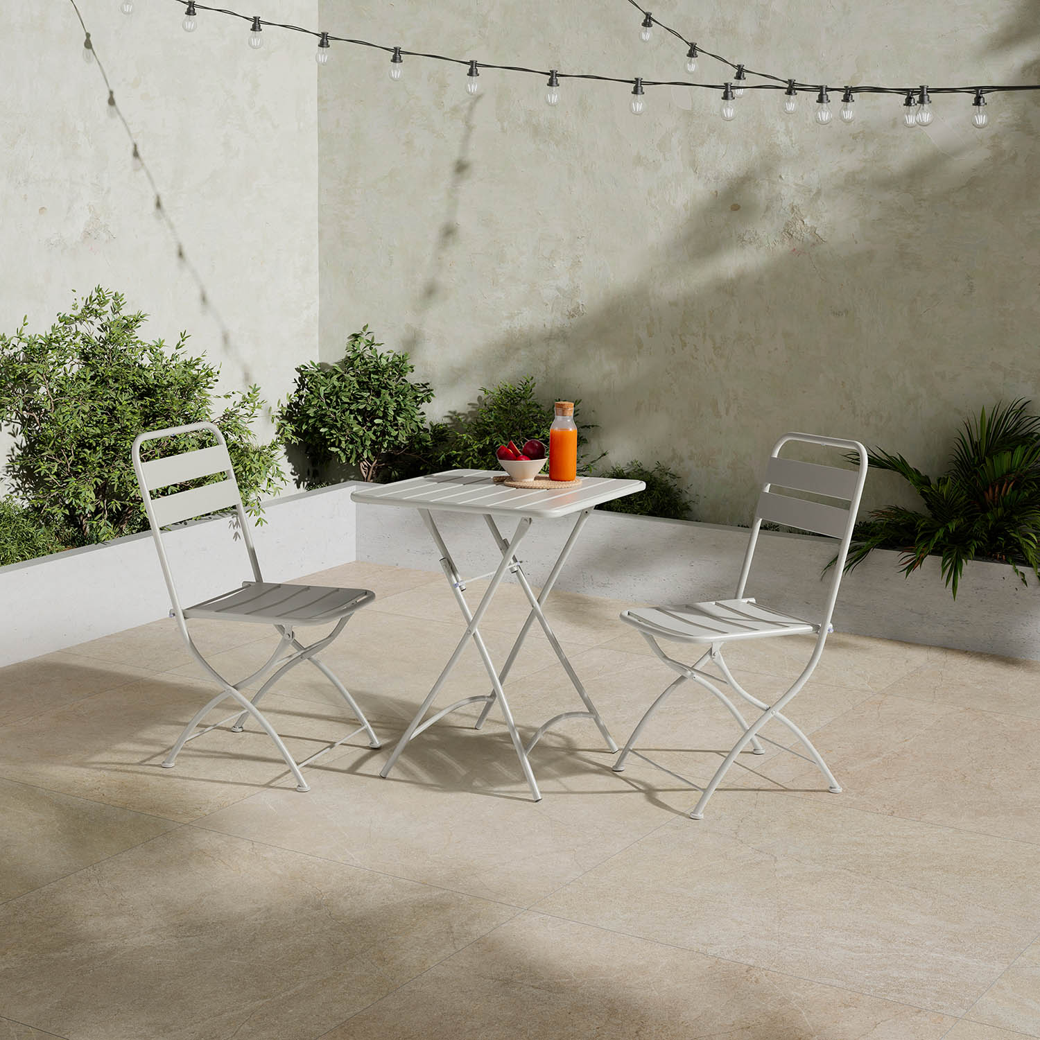 Una mesa de patio blanca con dos sillas, fruta y jugo al lado.