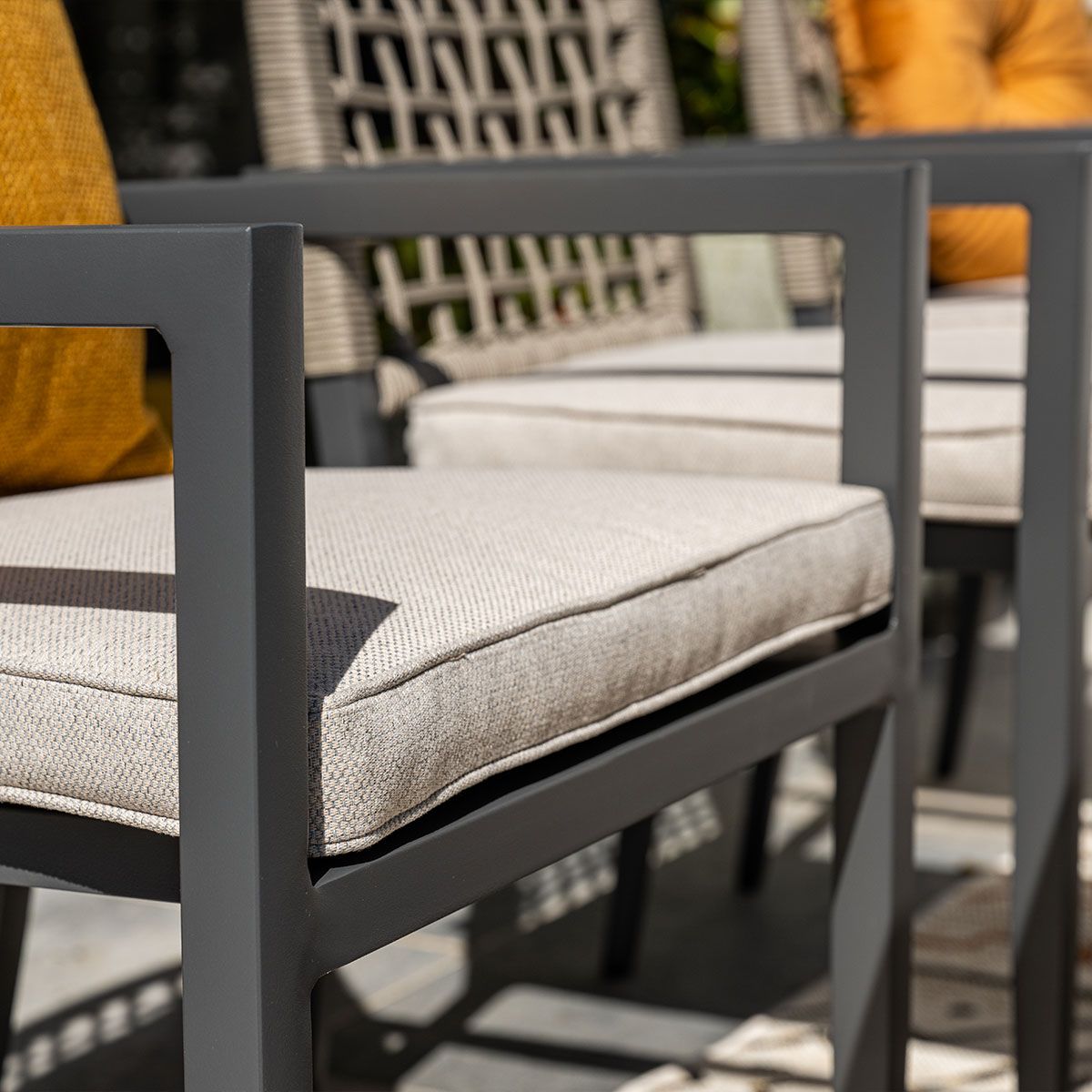 Drie donkere buitenstoelen met lichtbeige kussens en gele kussens.