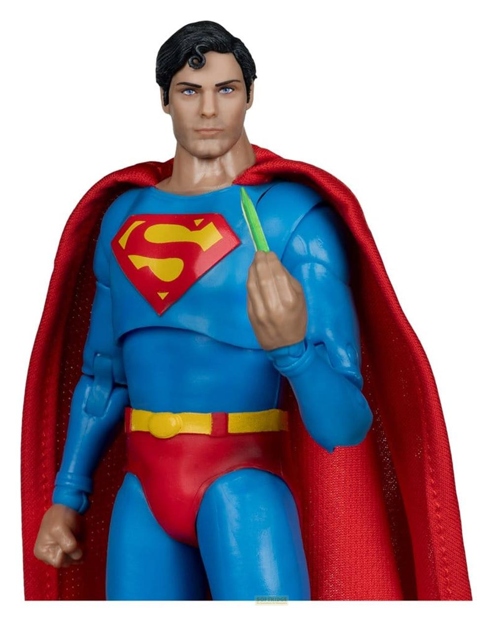 Eine Superman-Figur im blauen Anzug mit rotem Cape und gelbem Gürtel hält ein grünes Objekt.