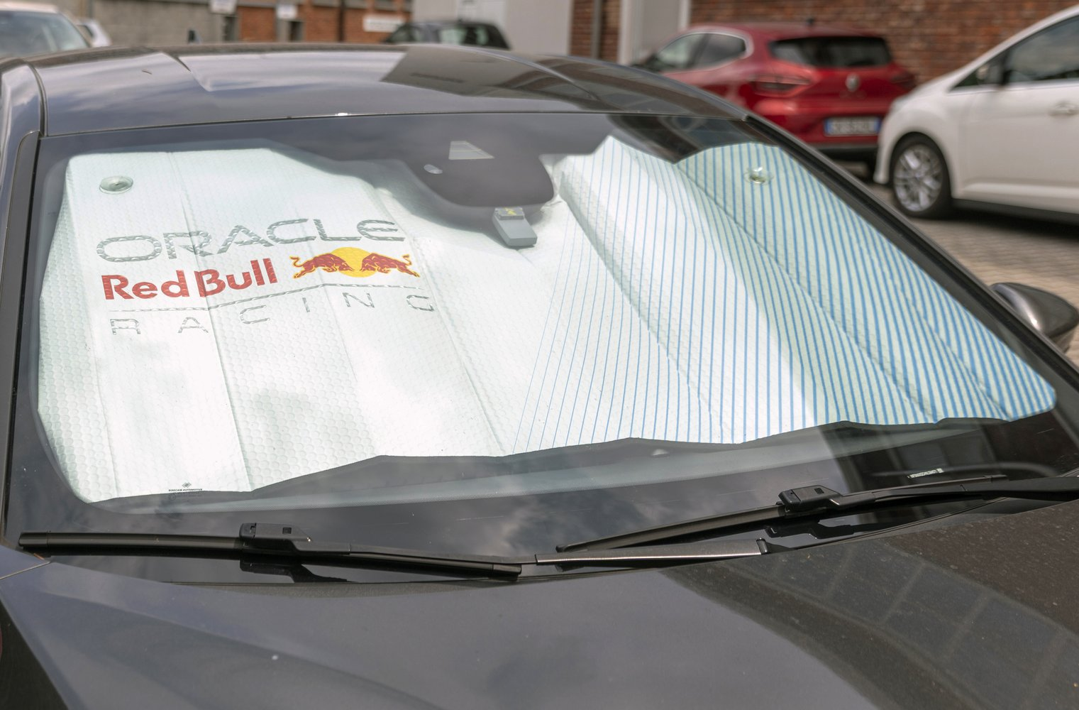 Parasole con logo Red Bull Racing all'interno di un'auto, auto parcheggiate fuori.