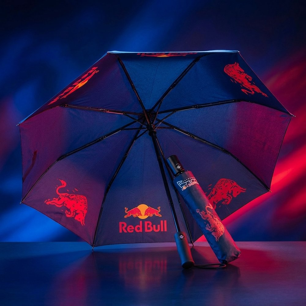 Un ombrello blu con loghi Red Bull e un motivo Red Bull. È aperto.