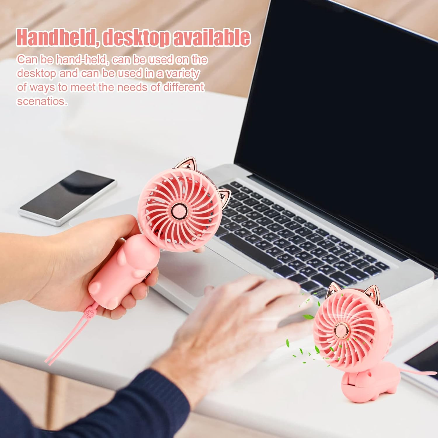 Eine Hand wird einen rosa Ventilator mit Katzenohren halten. Ein weiterer Ventilator steht auf einem Schreibtisch.