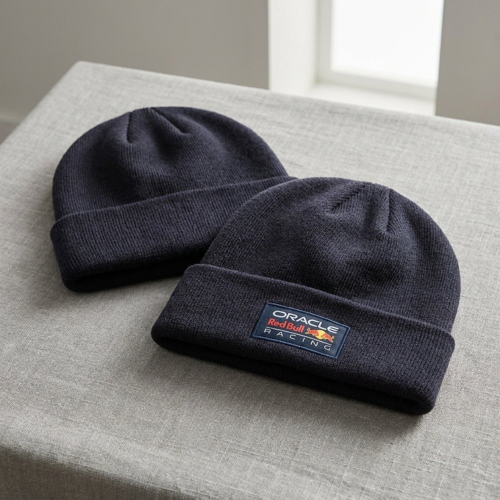 Due berretti blu scuro con logo Oracle Red Bull Racing su tessuto grigio.
