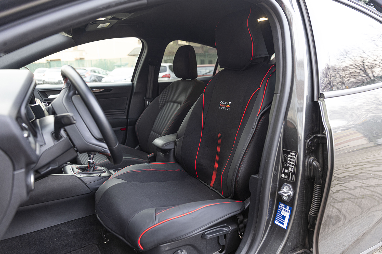 Interno auto con sedili sportivi, volante e leva del cambio. Accenti rossi.