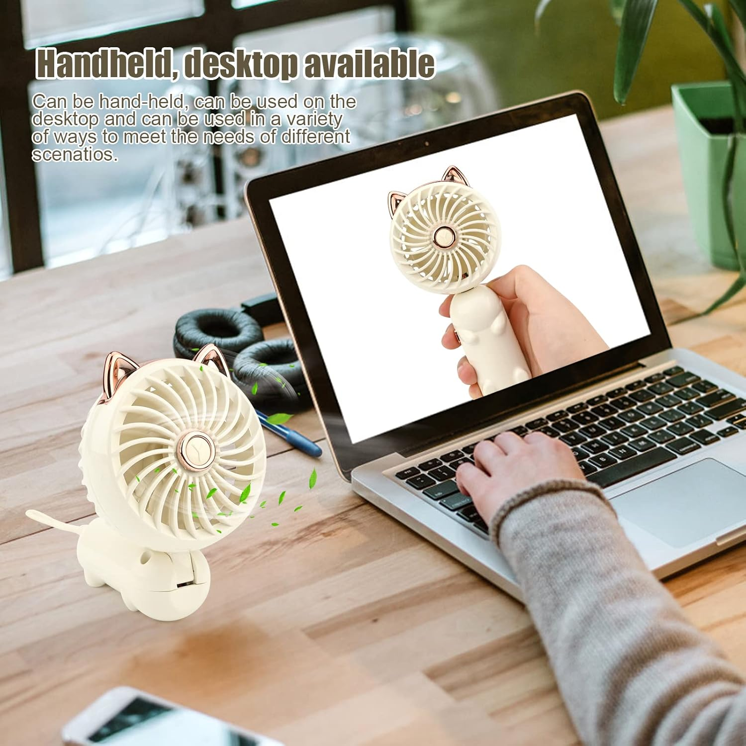 Ein handlicher Ventilator mit Katzenohren steht auf einem Schreibtisch neben einem Laptop.
