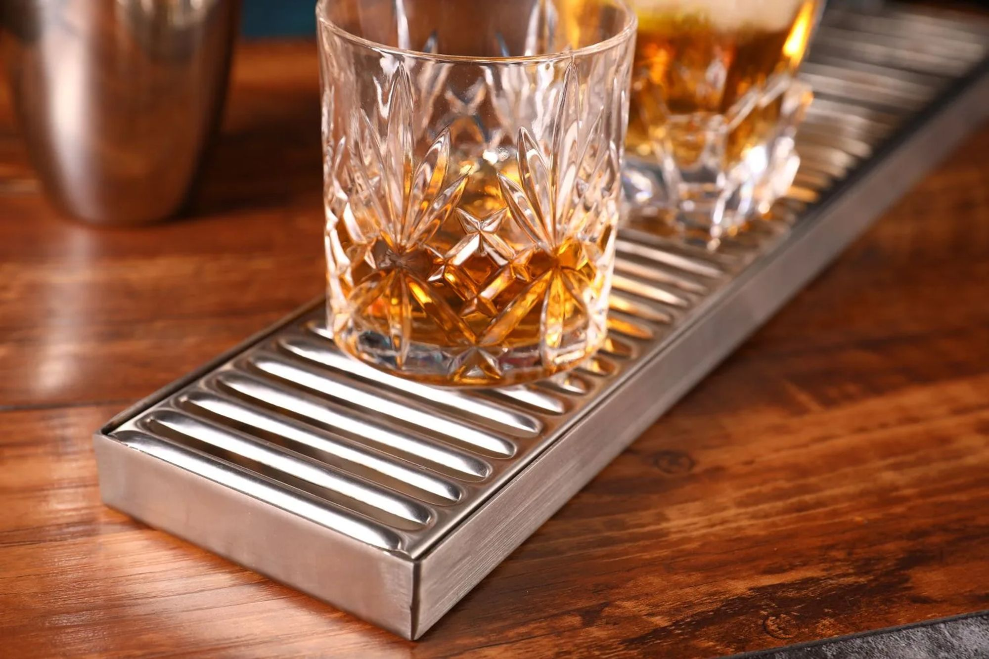 Two glasses with amber-colored drink on a ribbed metal tray.