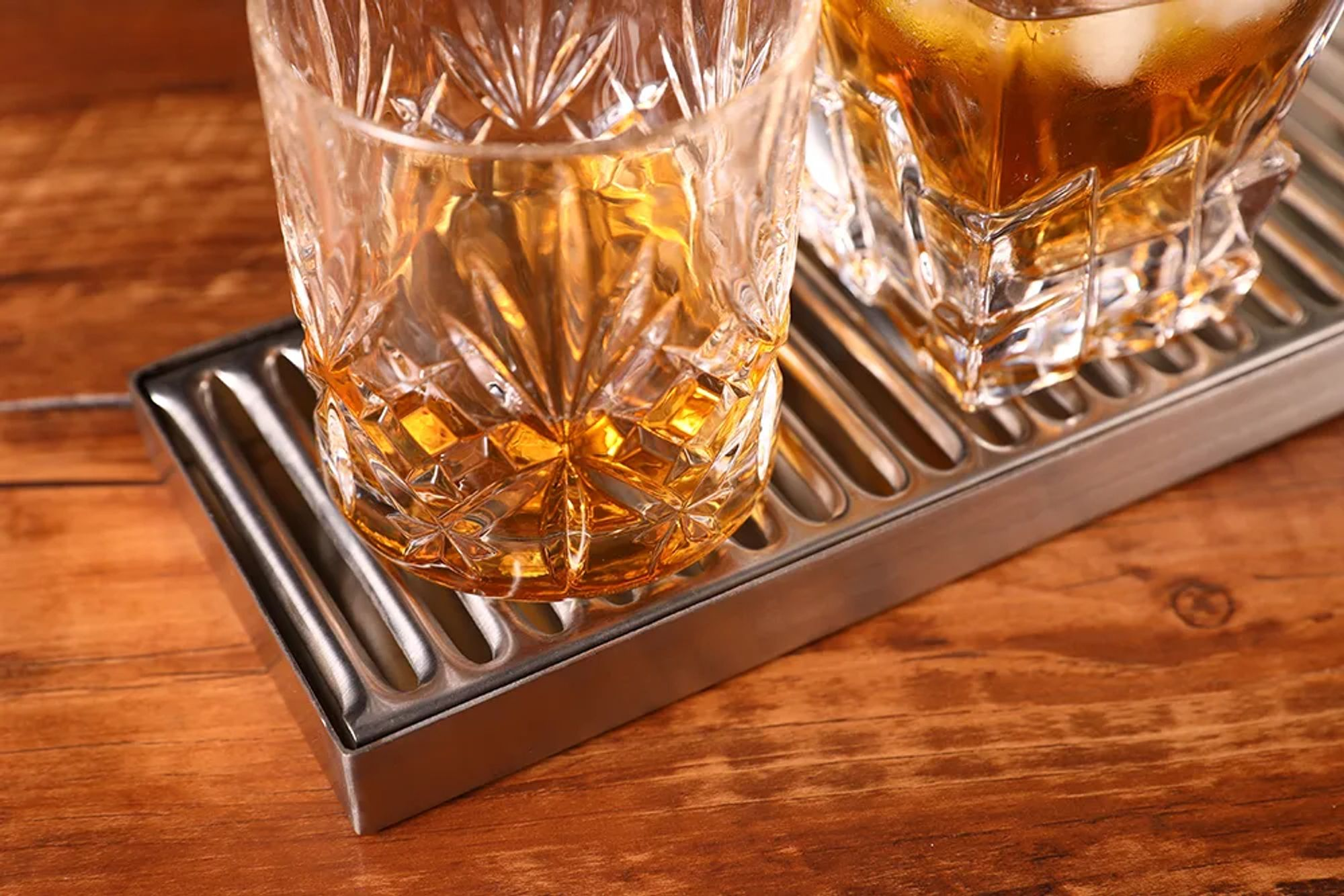 Two glasses with amber-colored drink and ice on a metal tray.