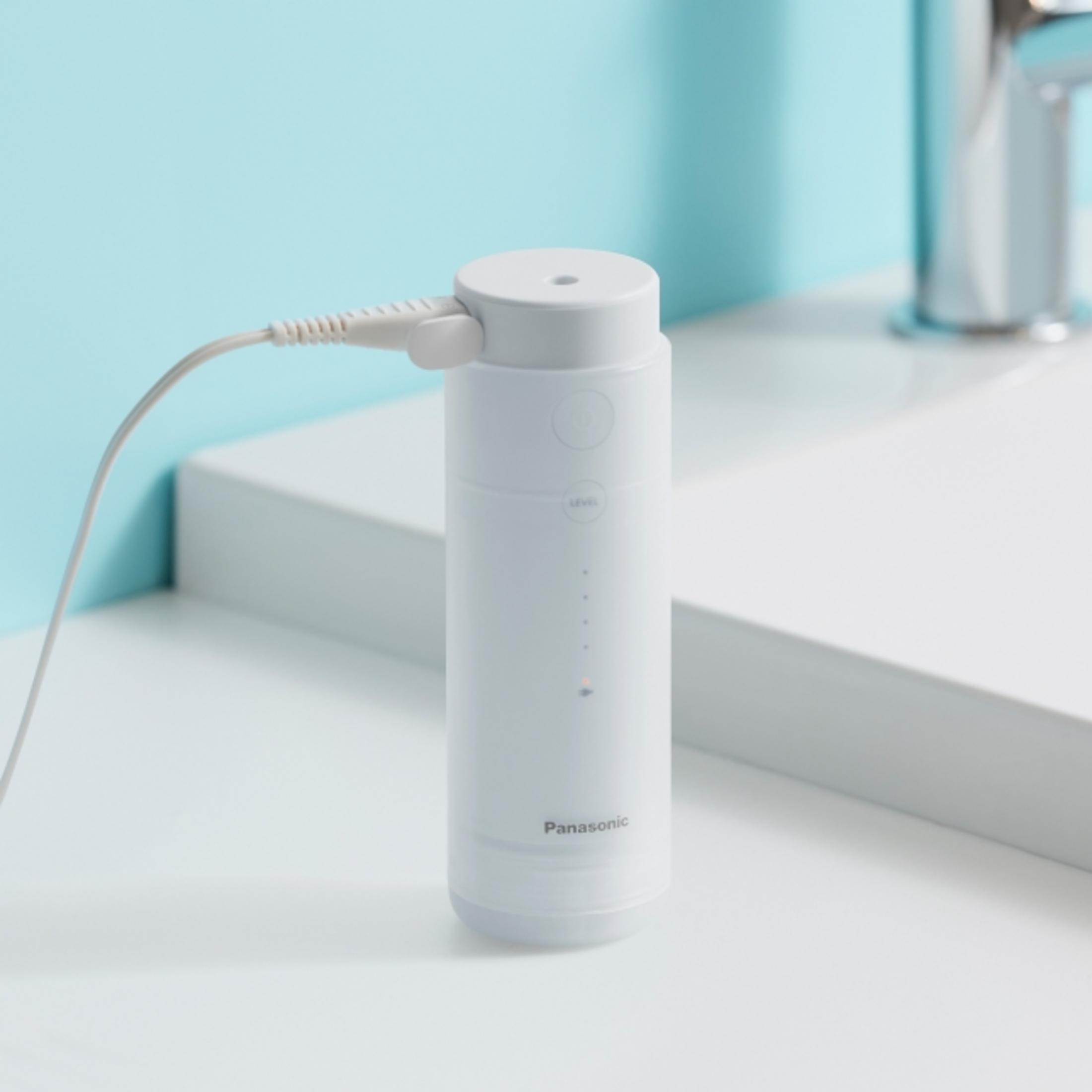 Ein weißer Panasonic Munddusche lädt auf weißer Fläche vor blauem Hintergrund.