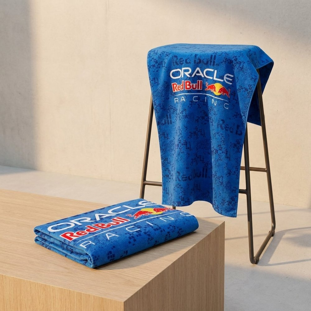Un asciugamano blu con logo Red Bull Racing giace su mobile di legno. Un altro è appeso a uno stand.