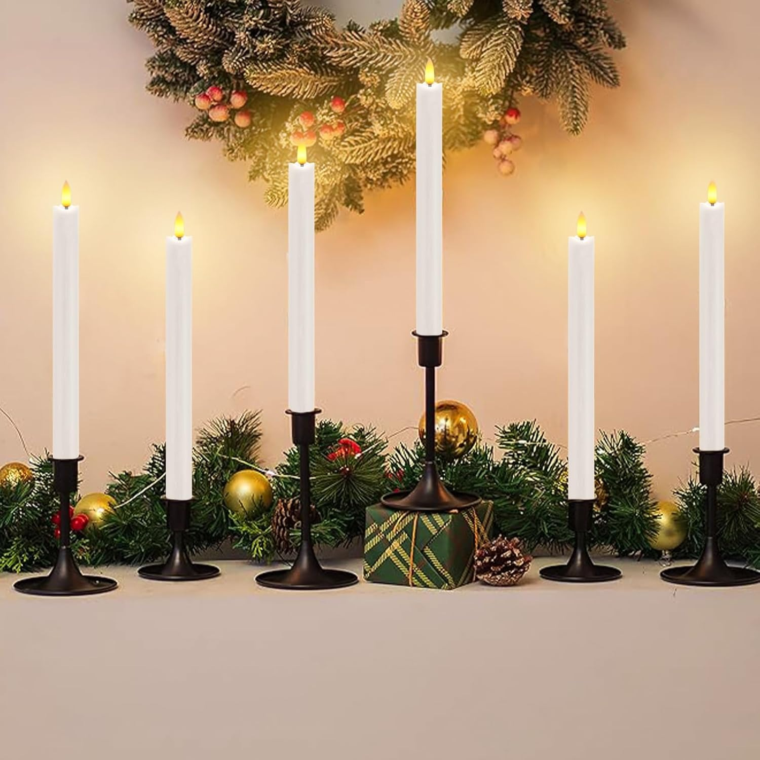 Sechs weiße Kerzen auf schwarzen Kerzenhaltern, mit Weihnachtsdeko.