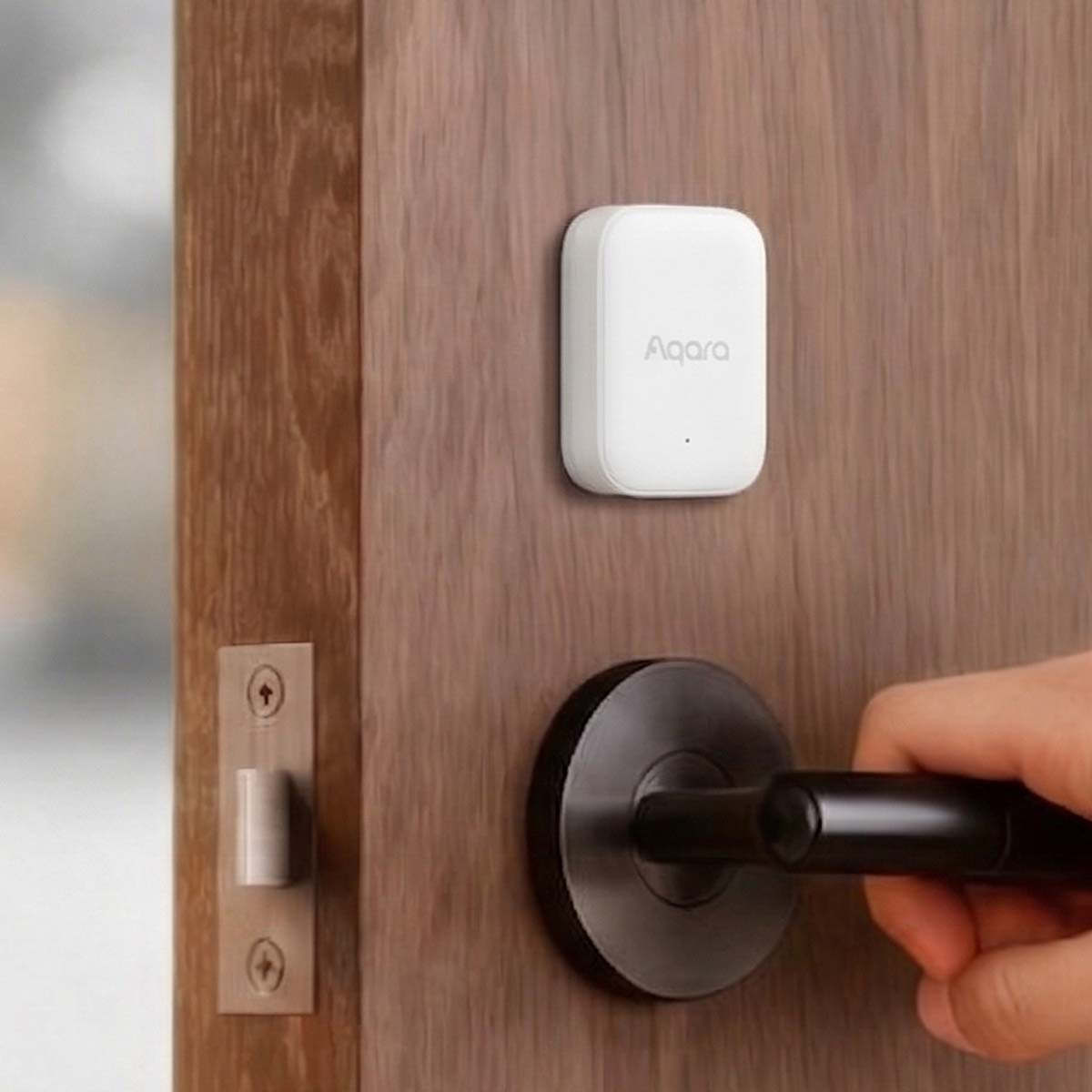Ein weißer Aqara-Sensor ist an einer Holztür befestigt. Eine Hand greift nach dem Türgriff.