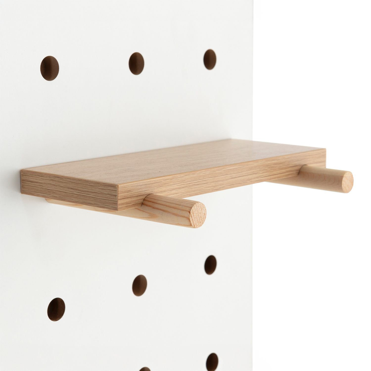 Una repisa de madera con clavijas de madera insertada en un tablero perforado blanco.