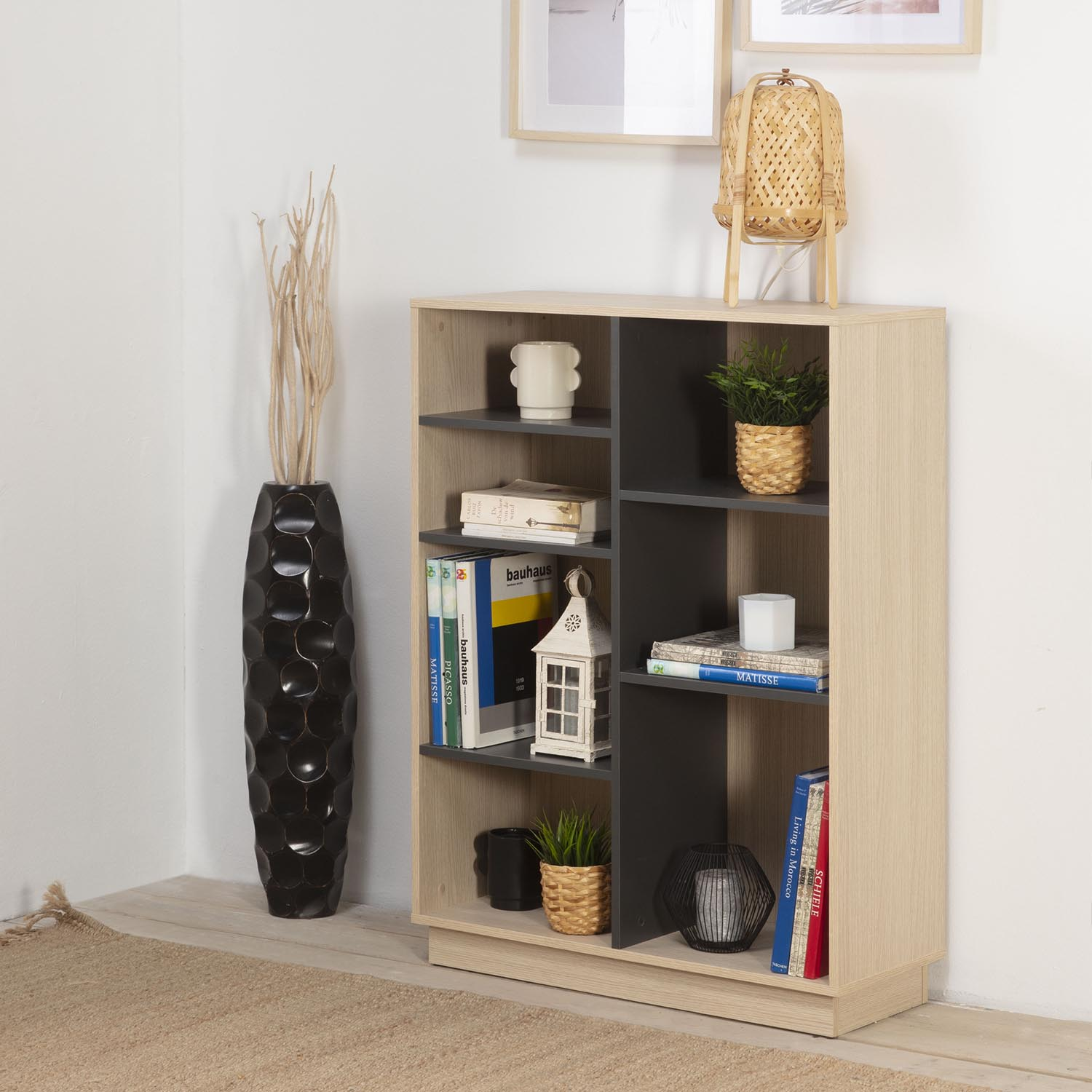 Una estantería con libros, plantas y objetos decorativos. Un jarrón negro a la izquierda.