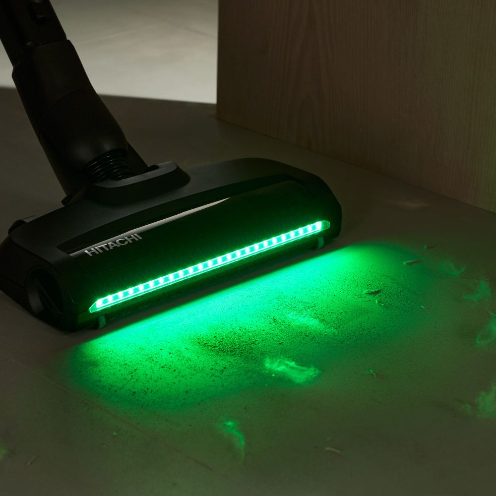 Ein schwarzer Staubsaugerkopf mit grüner LED-Beleuchtung auf staubigem Boden.