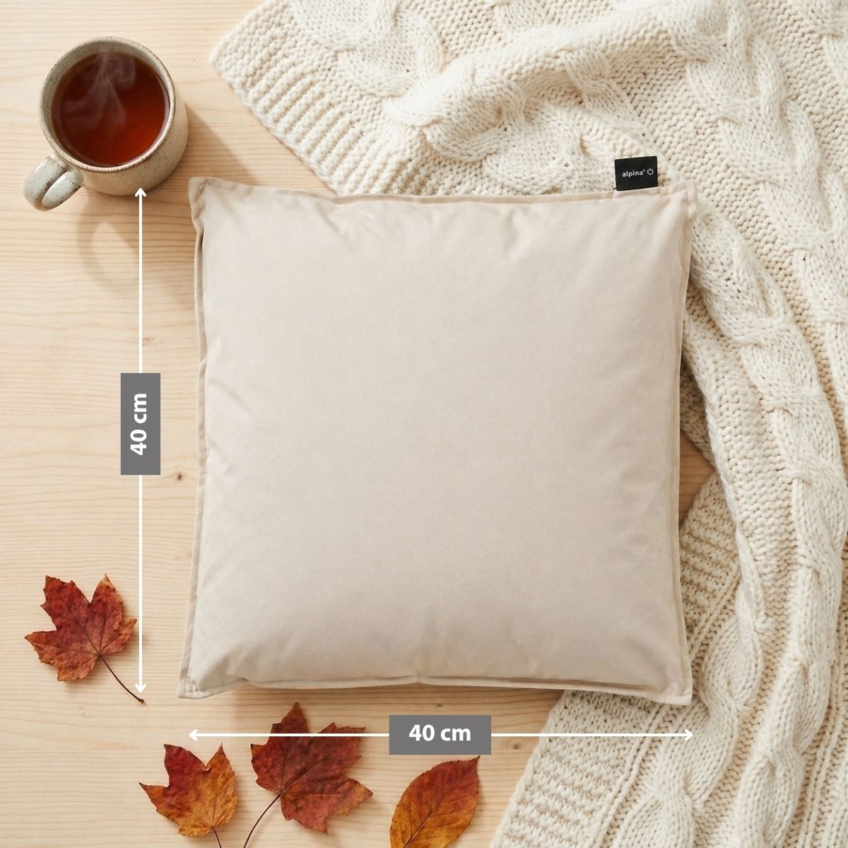 A beige 40x40cm pillow lies on a wooden table next to a cup of tea.