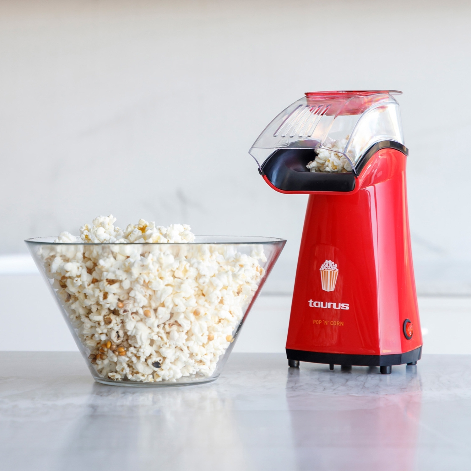 Una máquina de palomitas roja junto a un bol de cristal lleno de palomitas.