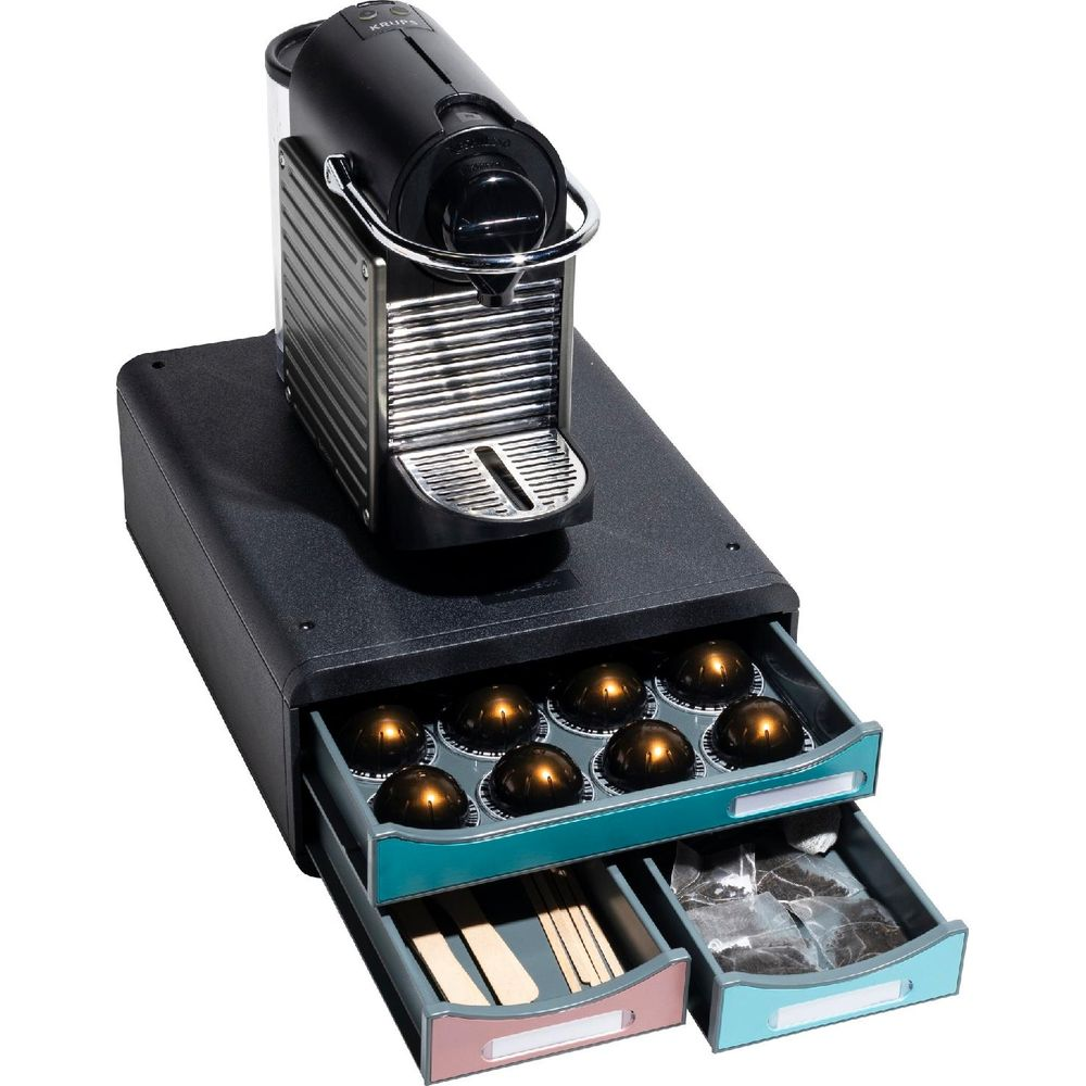 Una macchina per caffè a capsule poggia su un mobiletto nero con cassetti contenenti capsule e bustine di tè.