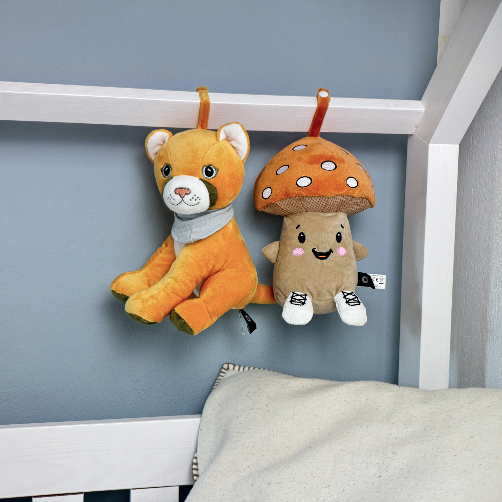 Ein orangefarbener Plüschlöwe und ein Pilz hängen an einem Bettgitter über einer Decke.
