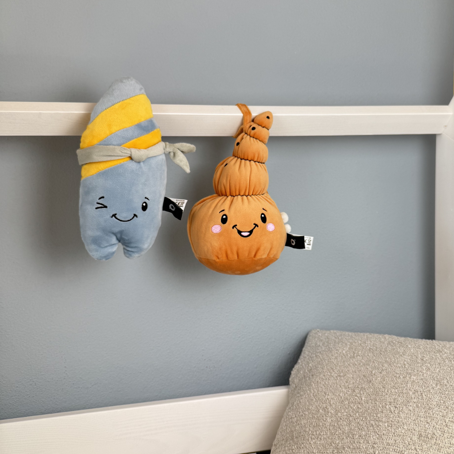 Zwei Plüschtiere, eines blau-gelb gestreift und das andere orange, hängen an einer Stange.