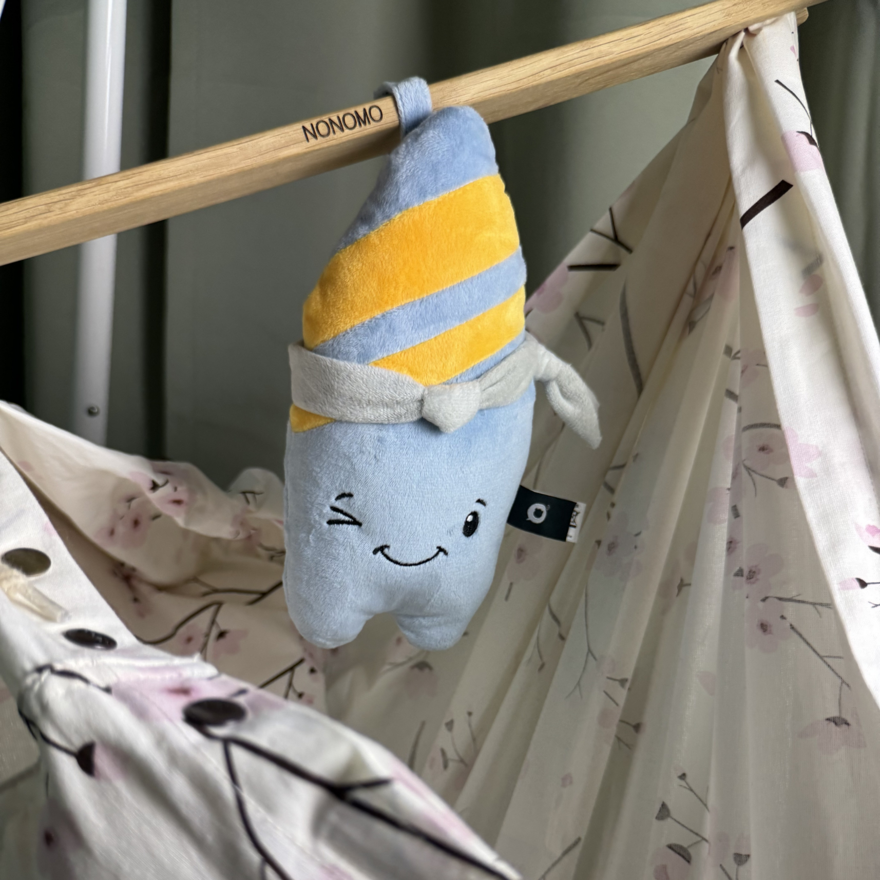 Ein blaues Stofftier mit gelben Streifen hängt an einer Holzstange über einem gemusterten Stoff.