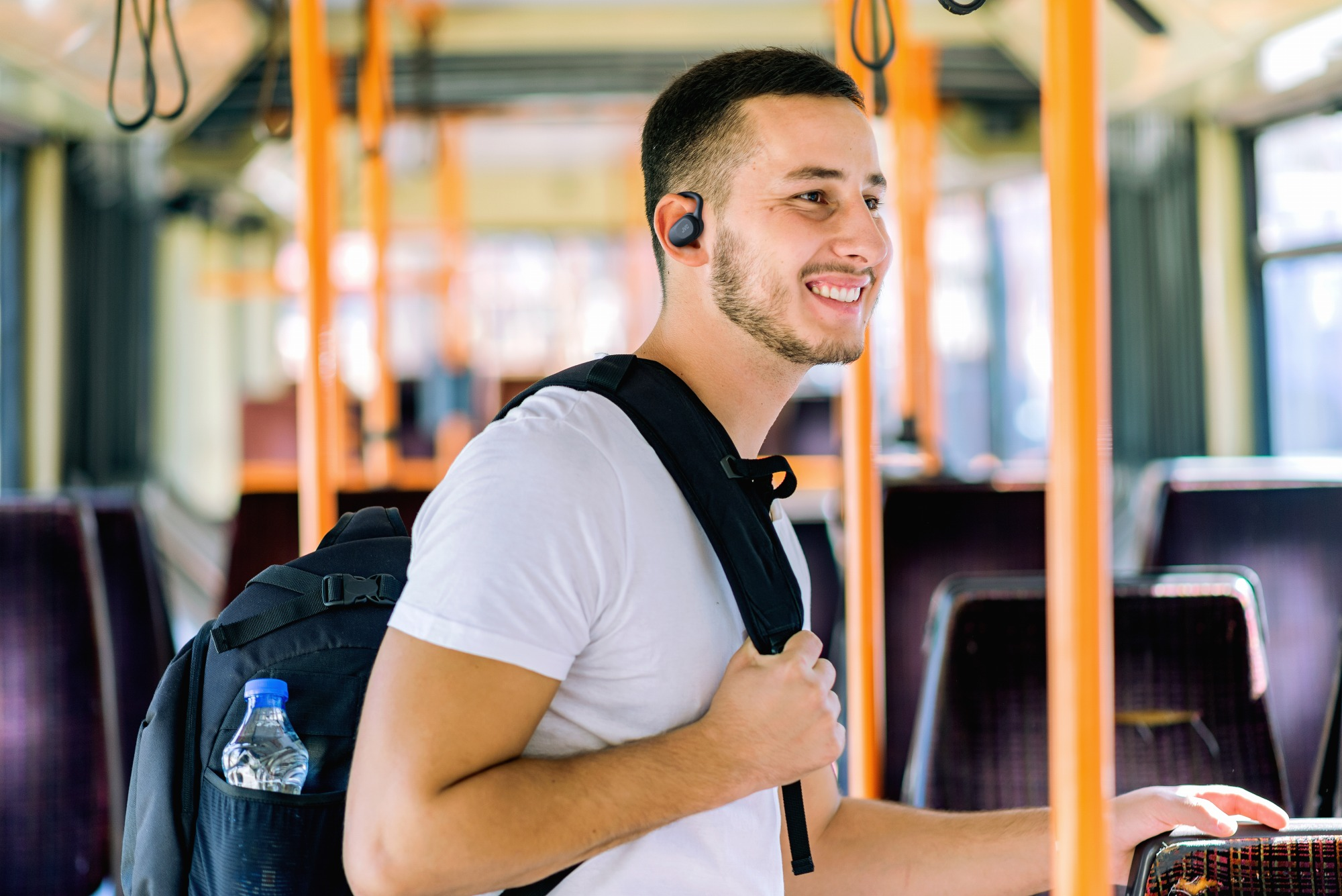 Un uomo con zaino e auricolari sorride su un autobus.