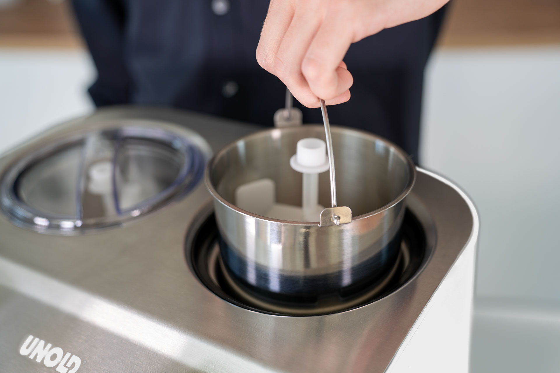 Eine Hand steckt ein Metallrührwerk in eine Edelstahlschüssel einer Eismaschine.