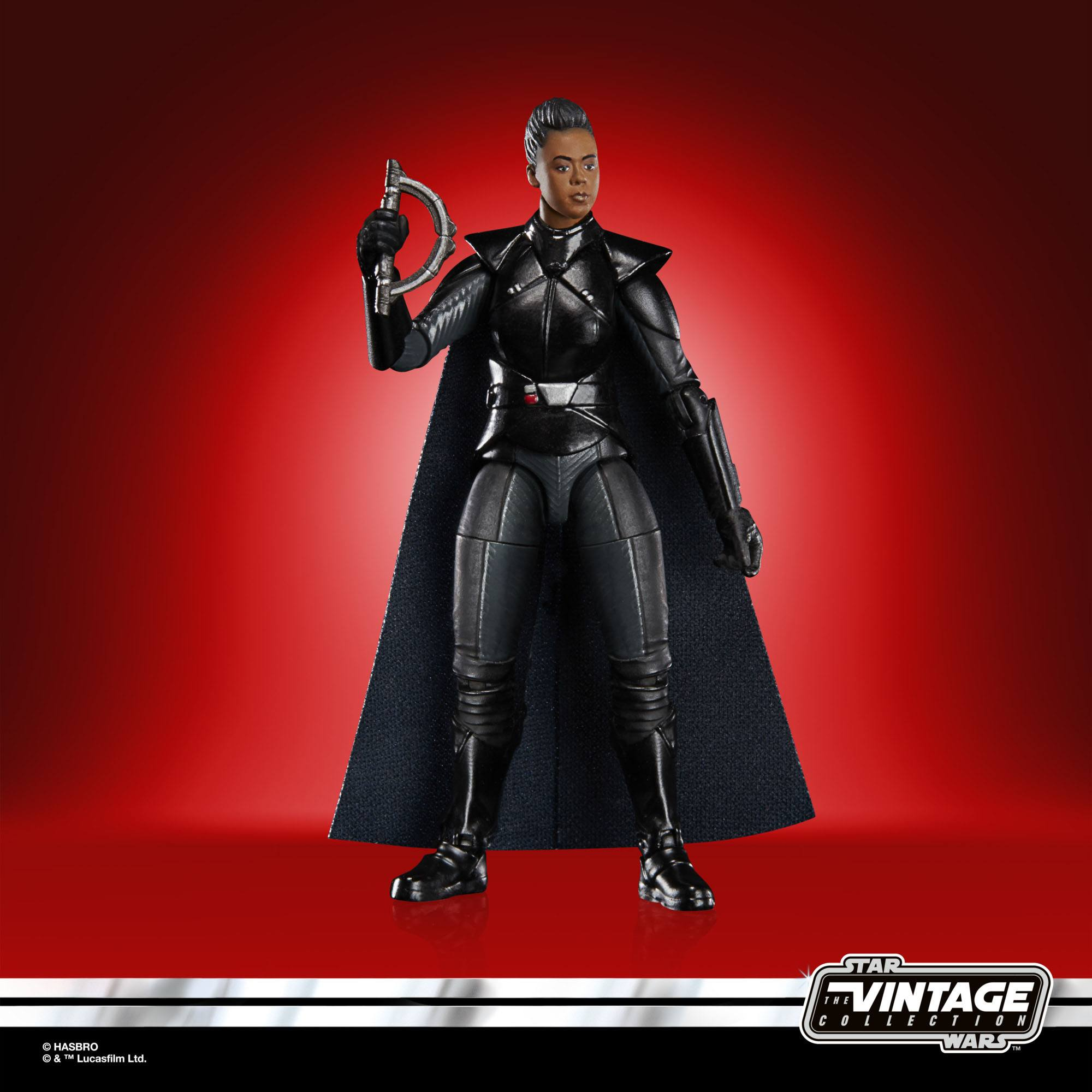 Action figure femminile in armatura nera tiene un'arma argentata su sfondo rosso.