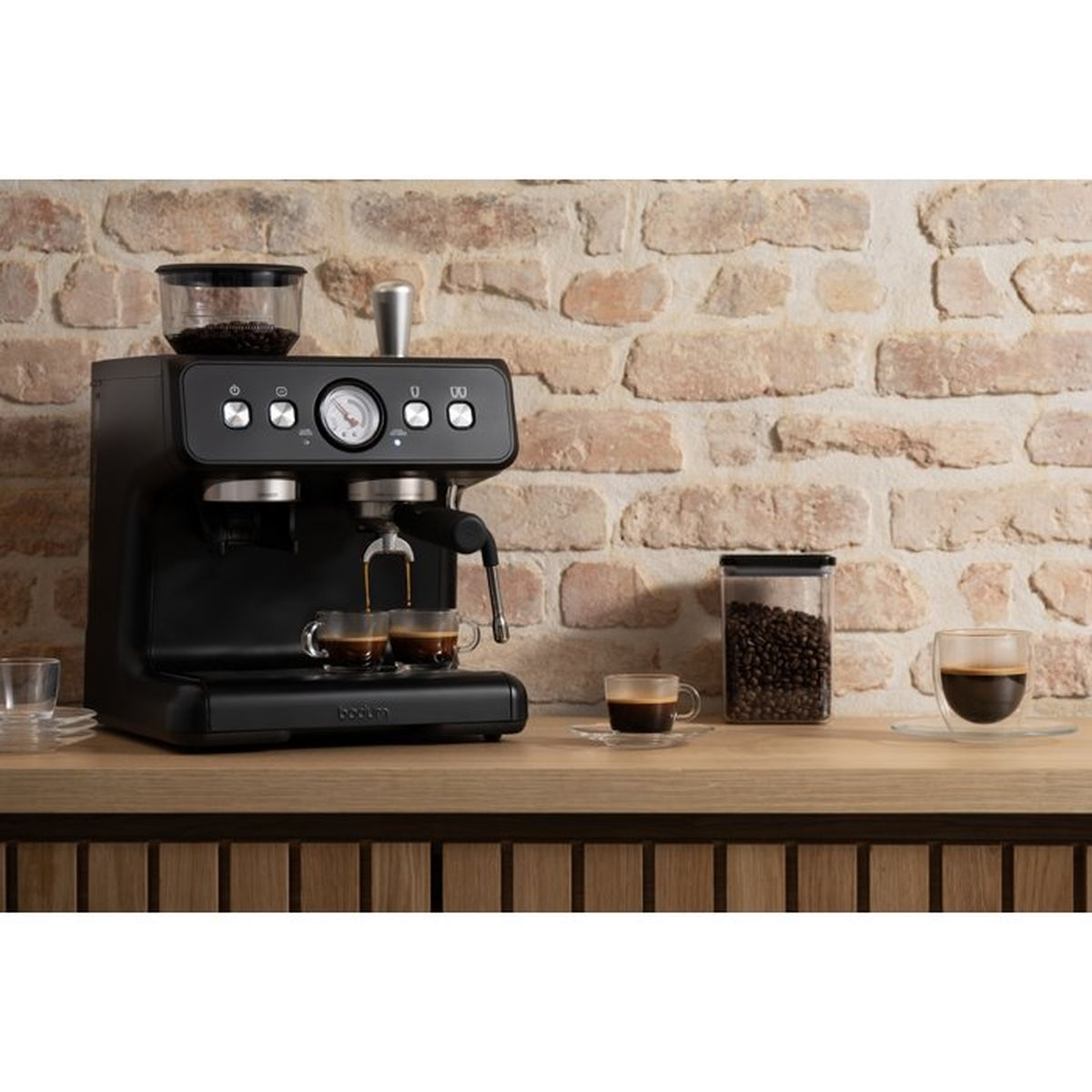 Macchina per espresso nera che prepara due tazze, con chicchi di caffè nelle vicinanze.