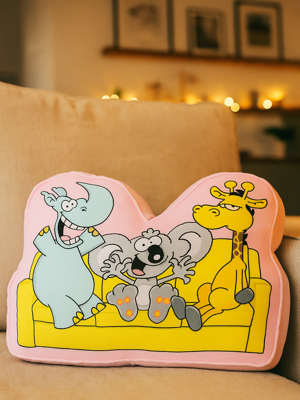 Ein rosa Kissen mit Zeichentricktieren: Nashorn, Koala und Giraffe auf einer gelben Couch.