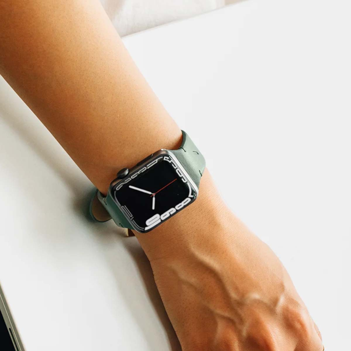 Osoba nosi smartwatch z zielonym paskiem na lewym nadgarstku na białym tle.