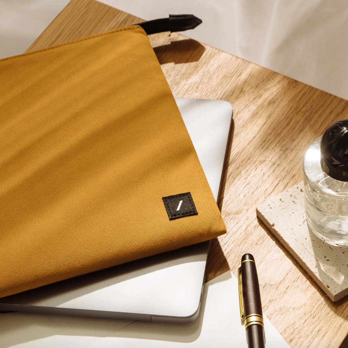Una pochette giallo senape su un laptop. Una penna e un bicchiere accanto.