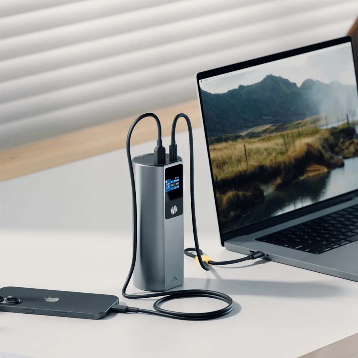 Power bank grigia carica un iPhone e un laptop su una scrivania.