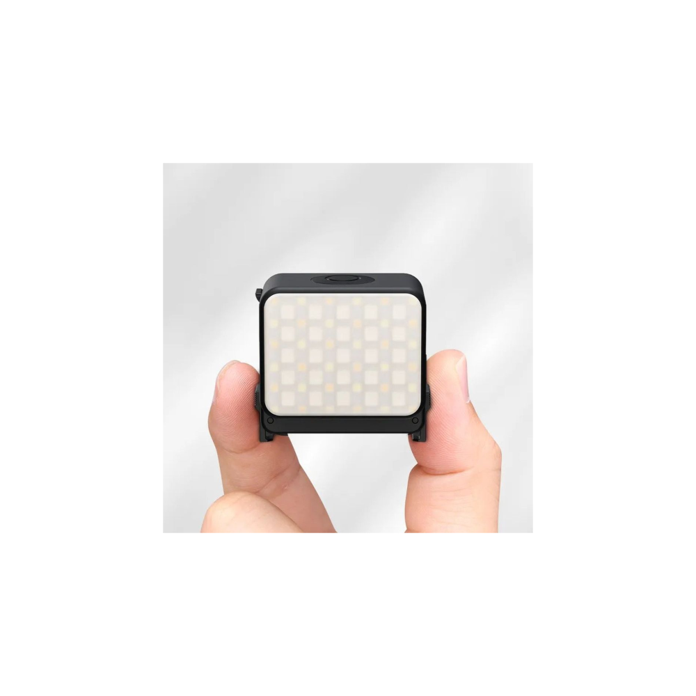 Een hand houdt een klein, rechthoekig zwart LED-lampje met veel lampjes vast.