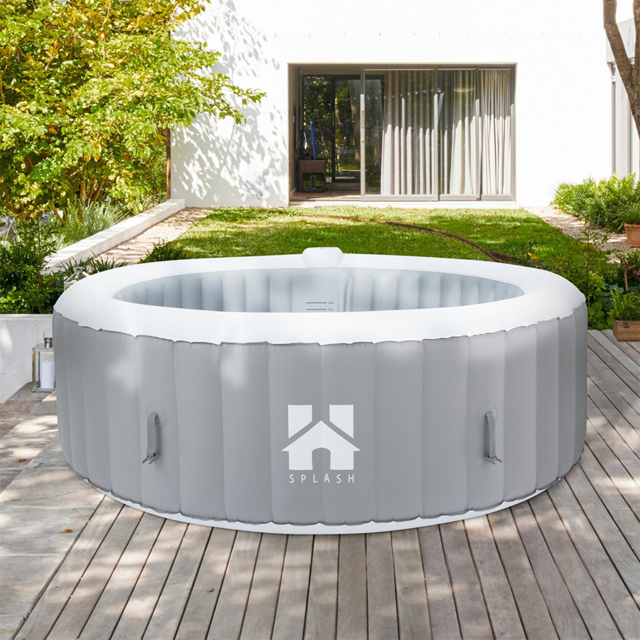 Auf einer Holzterrasse steht ein aufblasbarer Whirlpool. Im Hintergrund ist ein Haus mit Fenstern und Grünpflanzen.