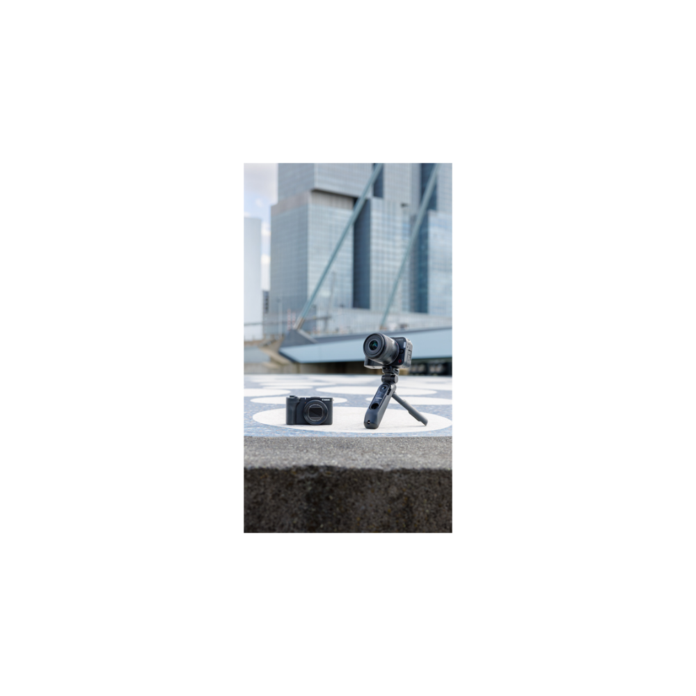 Two cameras sit outdoors, one on a tripod, with modern buildings in the background.