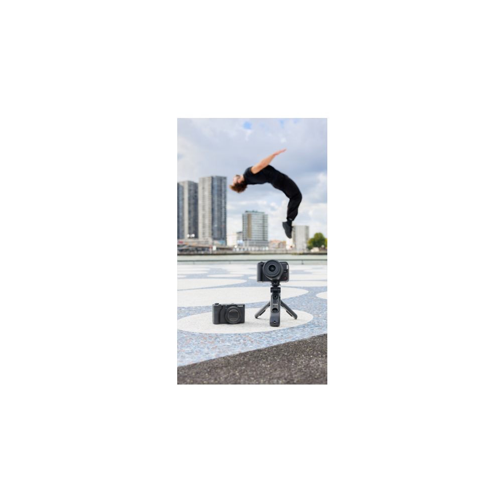 A man does a backflip in front of cameras with city buildings behind.