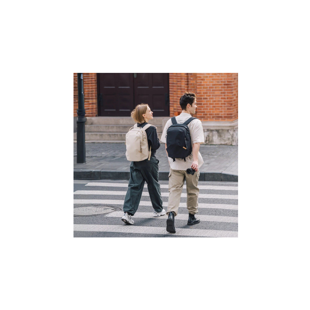 A man and woman cross a street on a crosswalk. They are wearing backpacks.