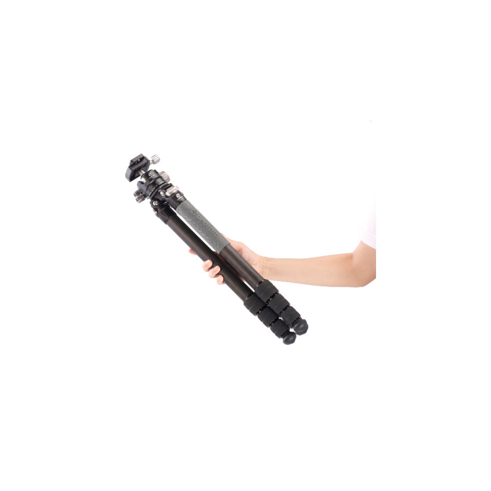 A hand holds a dark tripod with silver clamps and a head.