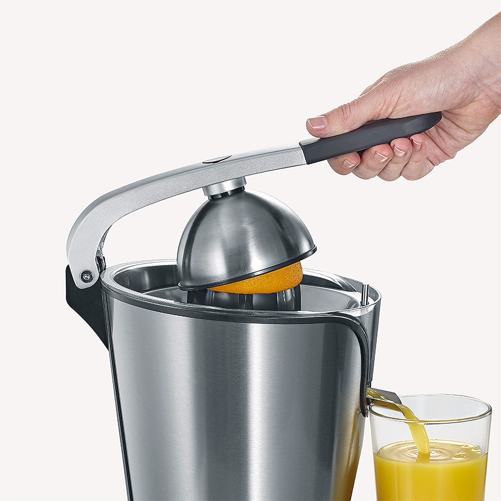 Mano preme la leva dello spremiagrumi, arancia spremuta, succo scorre nel bicchiere.