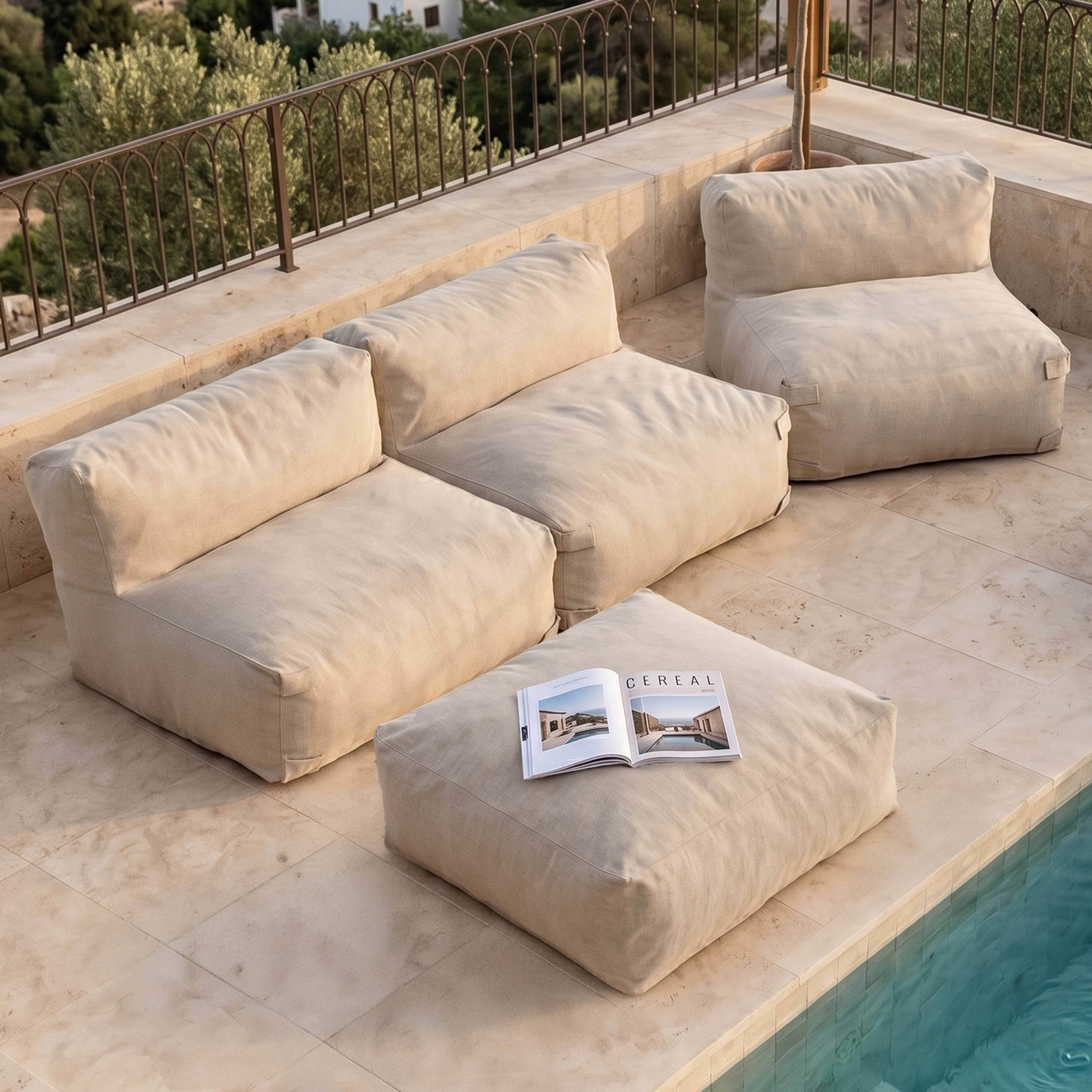 Beige Loungemöbel und ein Magazin am Poolrand auf einer Steinterrasse.
