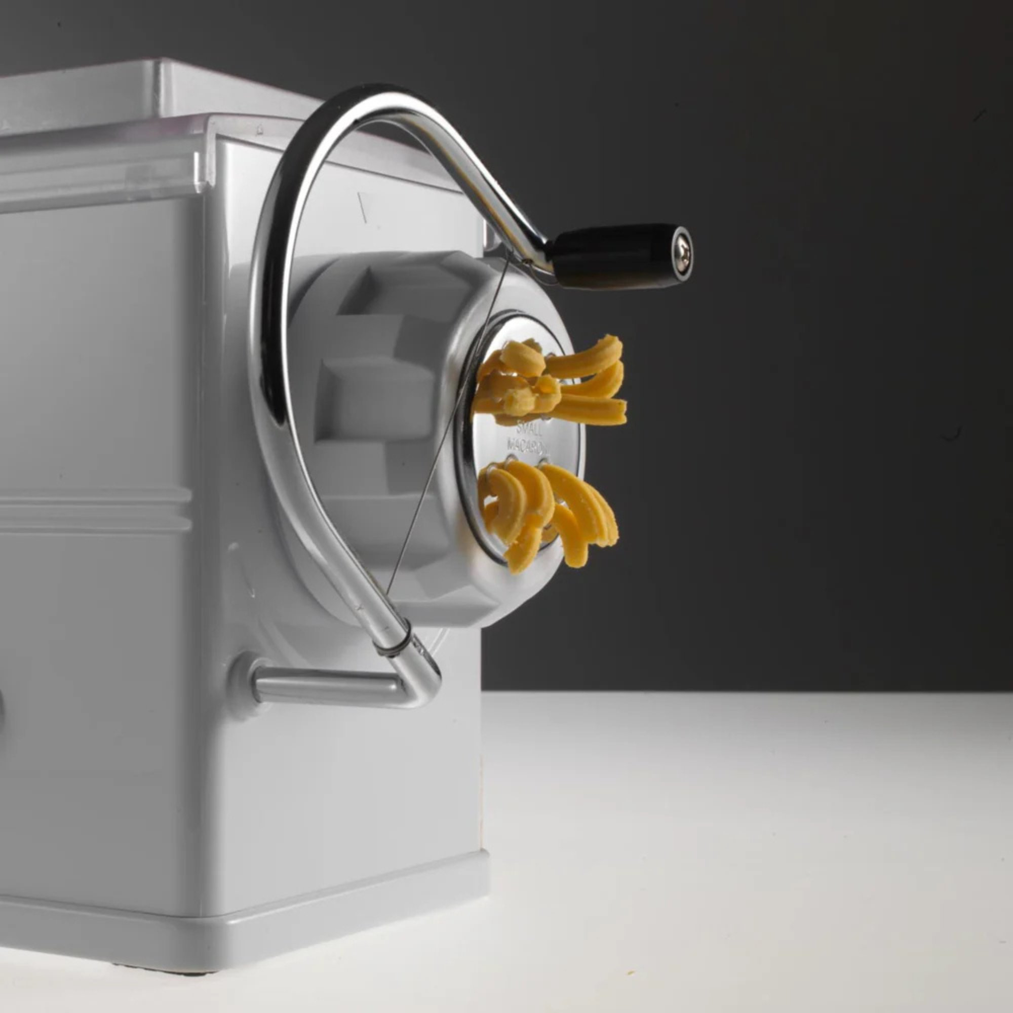 Eine weiße Nudelmaschine mit einem silbernen Griff und frisch zubereiteter Pasta.