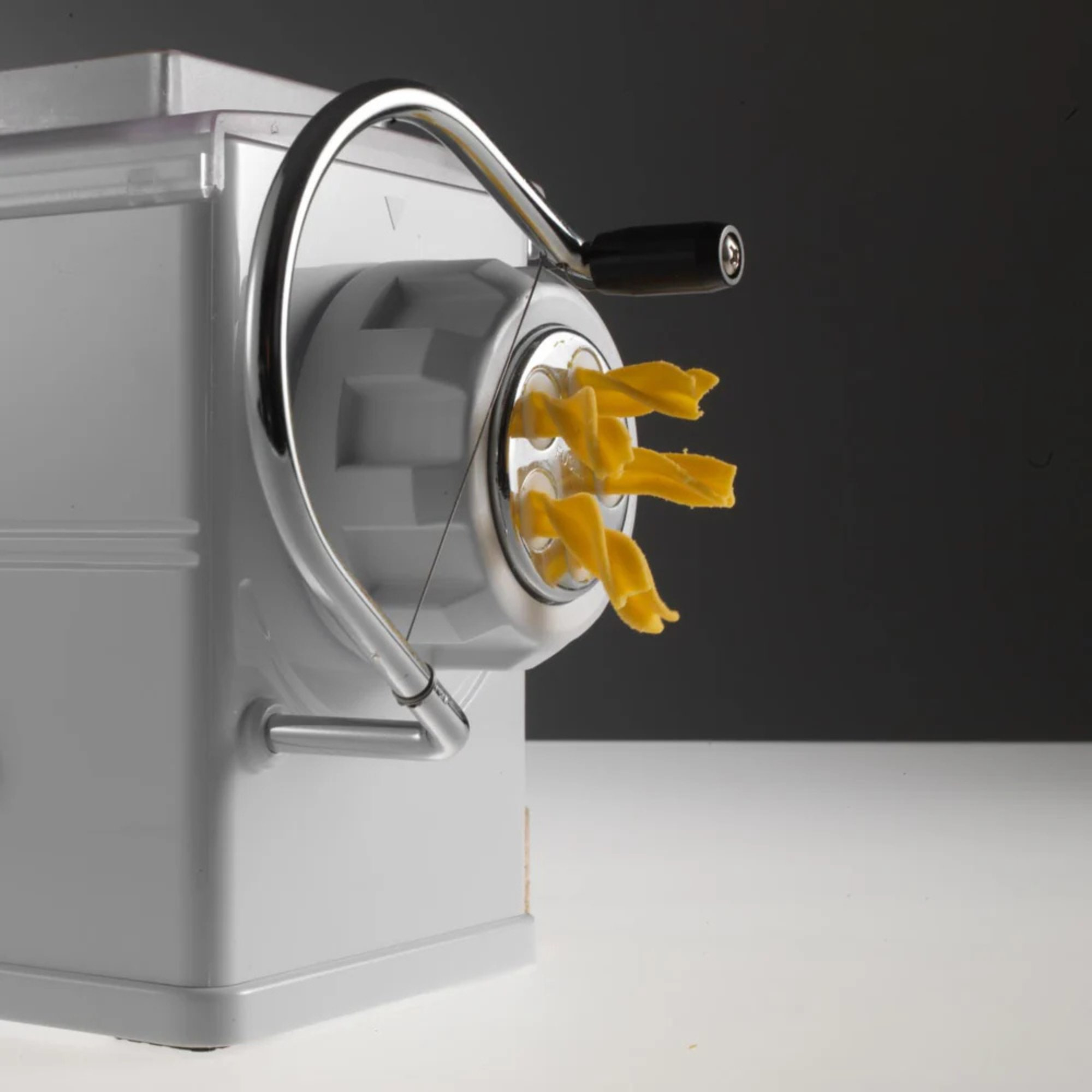 Eine weiße Nudelmaschine mit silbernem Griff und frisch extrudierten gelben Nudeln.