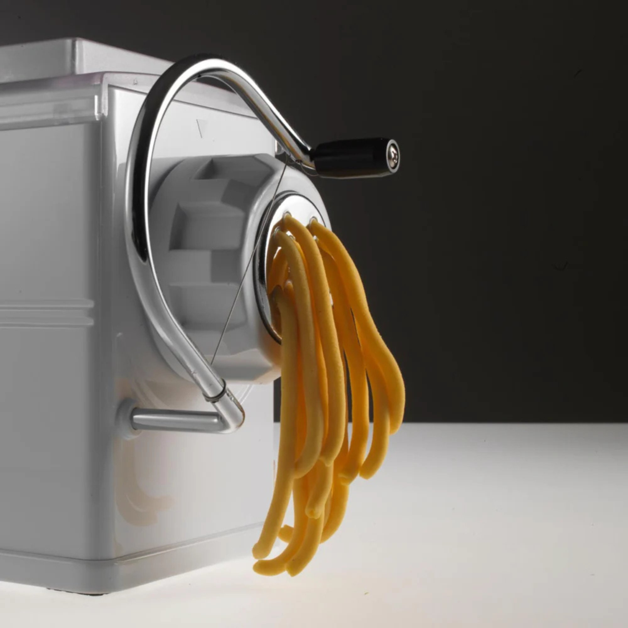 Eine weiße Nudelmaschine mit glänzendem Hebel, frische Pasta hängt heraus.
