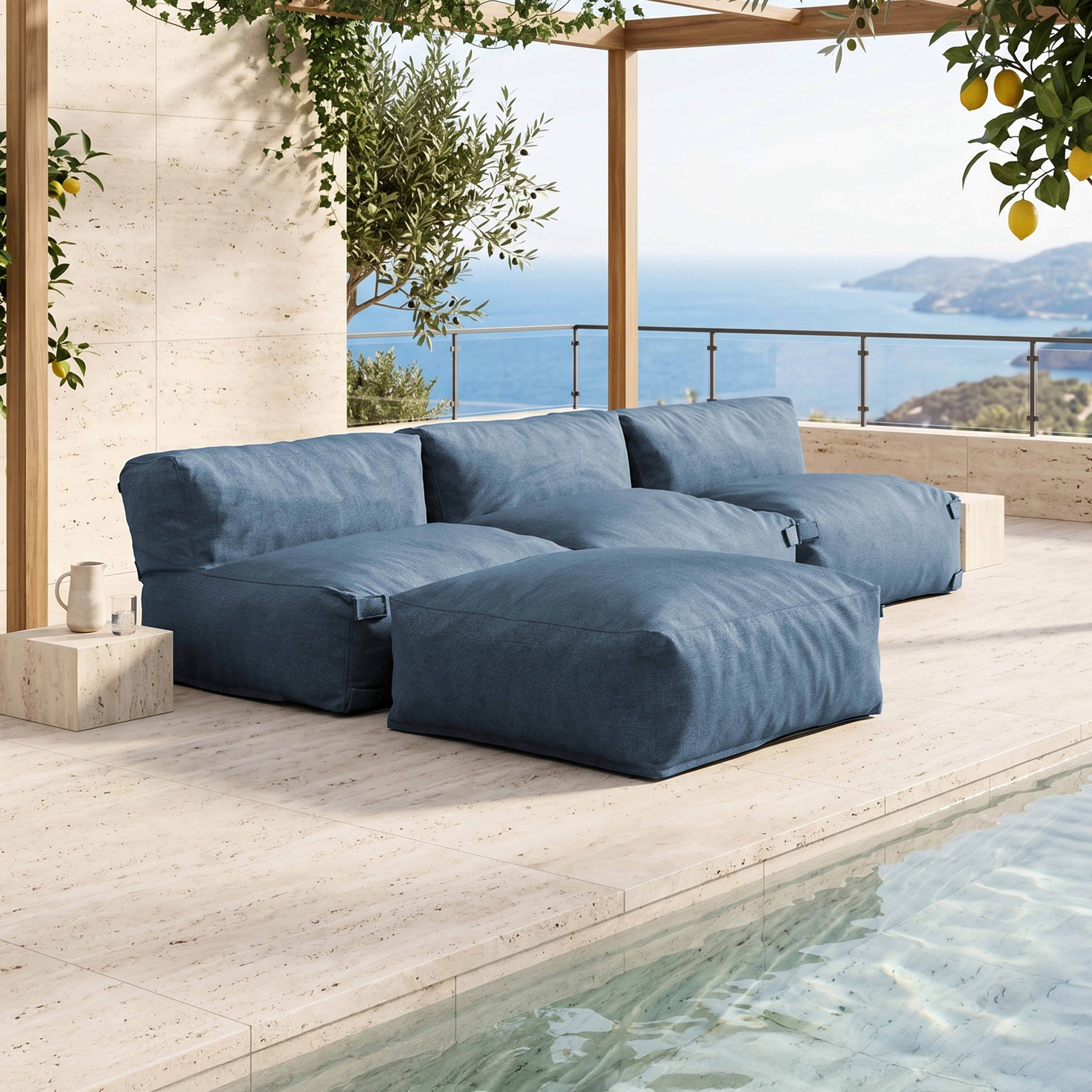 Ein blaues Loungesofa und ein Hocker stehen auf einer gefliesten Terrasse am Meer.