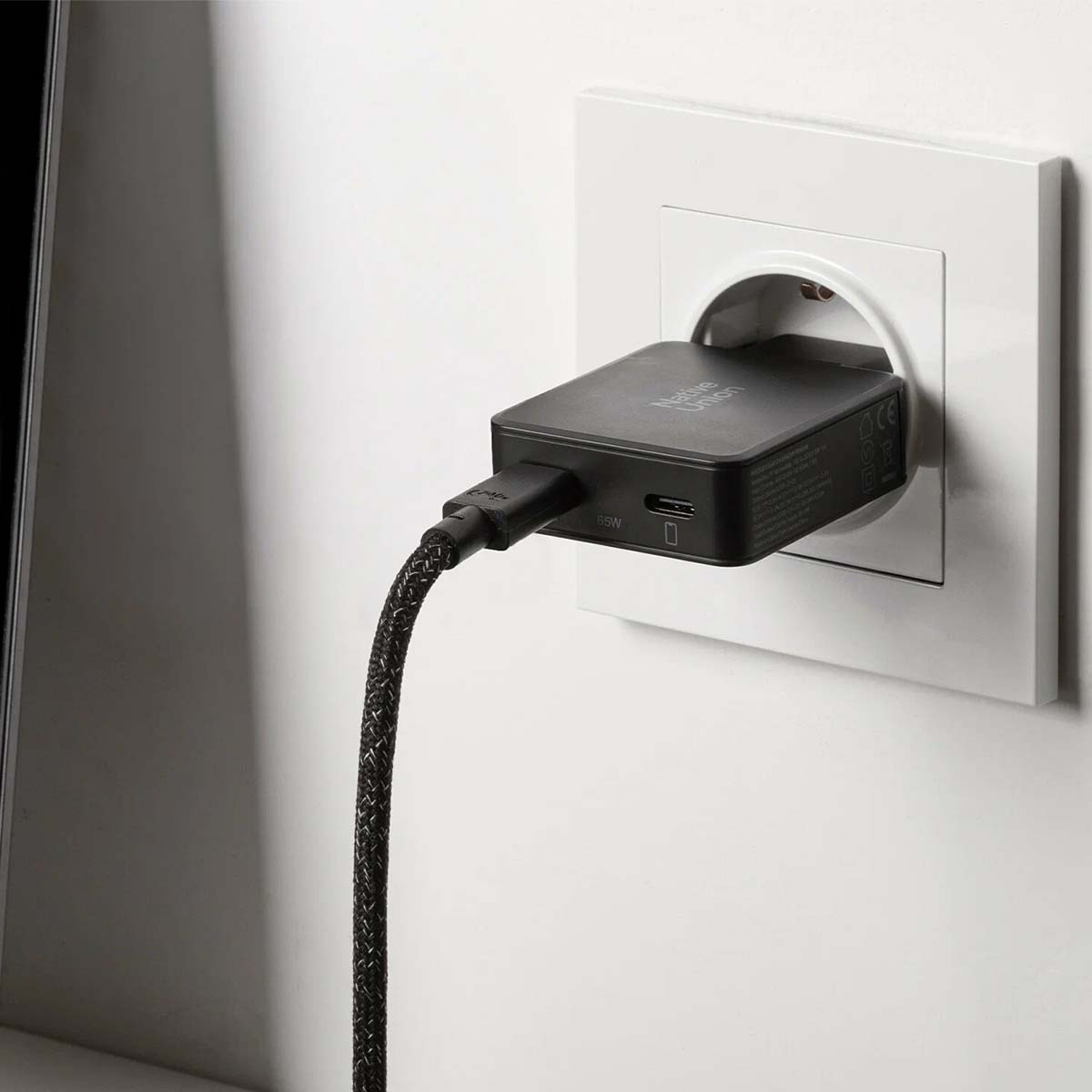Ein schwarzes Native Union Ladegerät steckt in einer weißen Steckdose. Ein schwarzes Kabel ragt heraus.