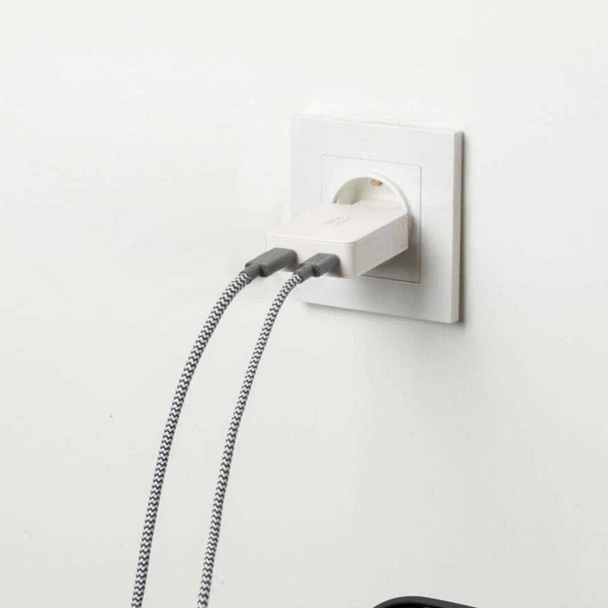 Ein weißer Ladestecker mit zwei schwarz-weißen Kabeln steckt in einer weißen Steckdose.