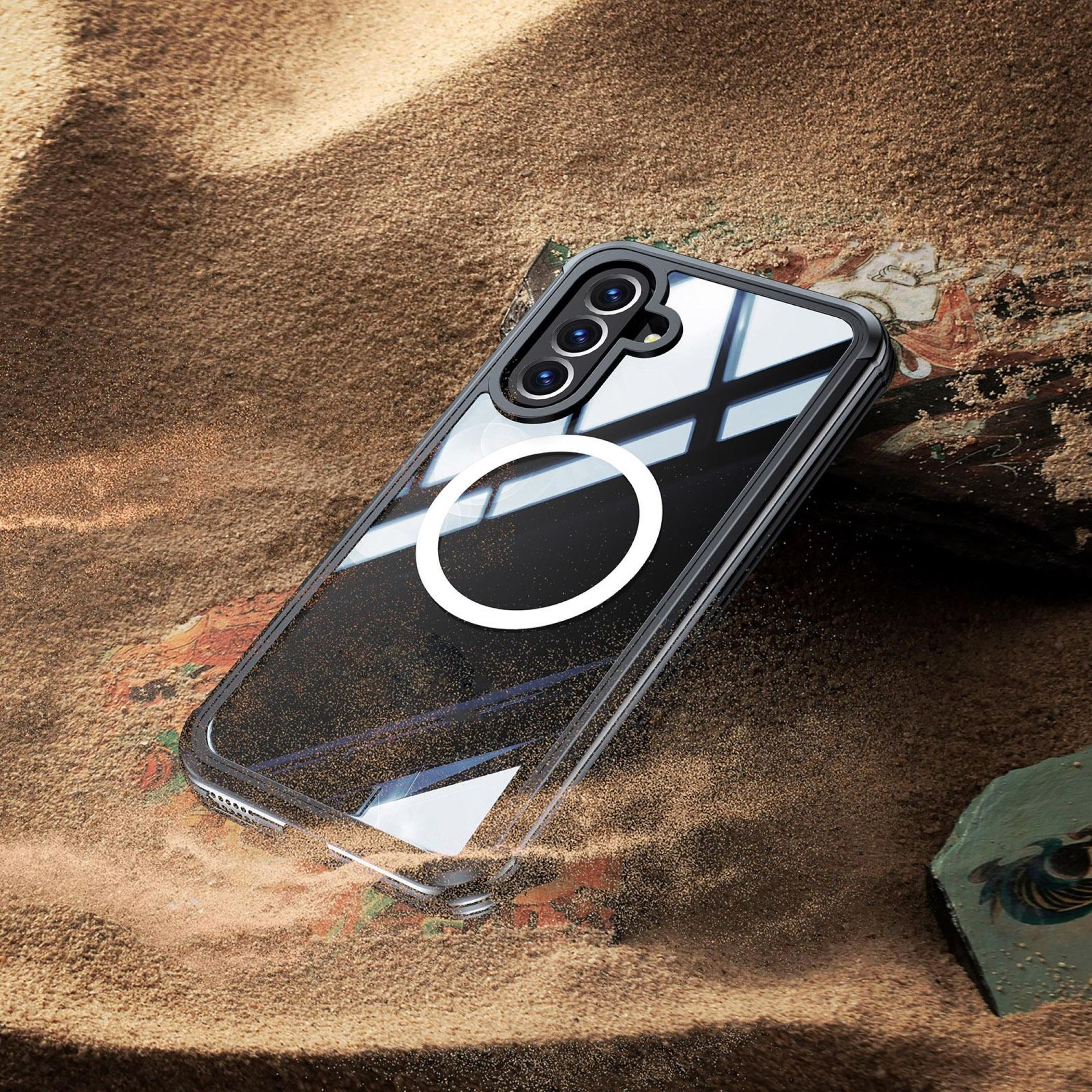 Un telefono nero con tre fotocamere poggia su sabbia e tessuto.