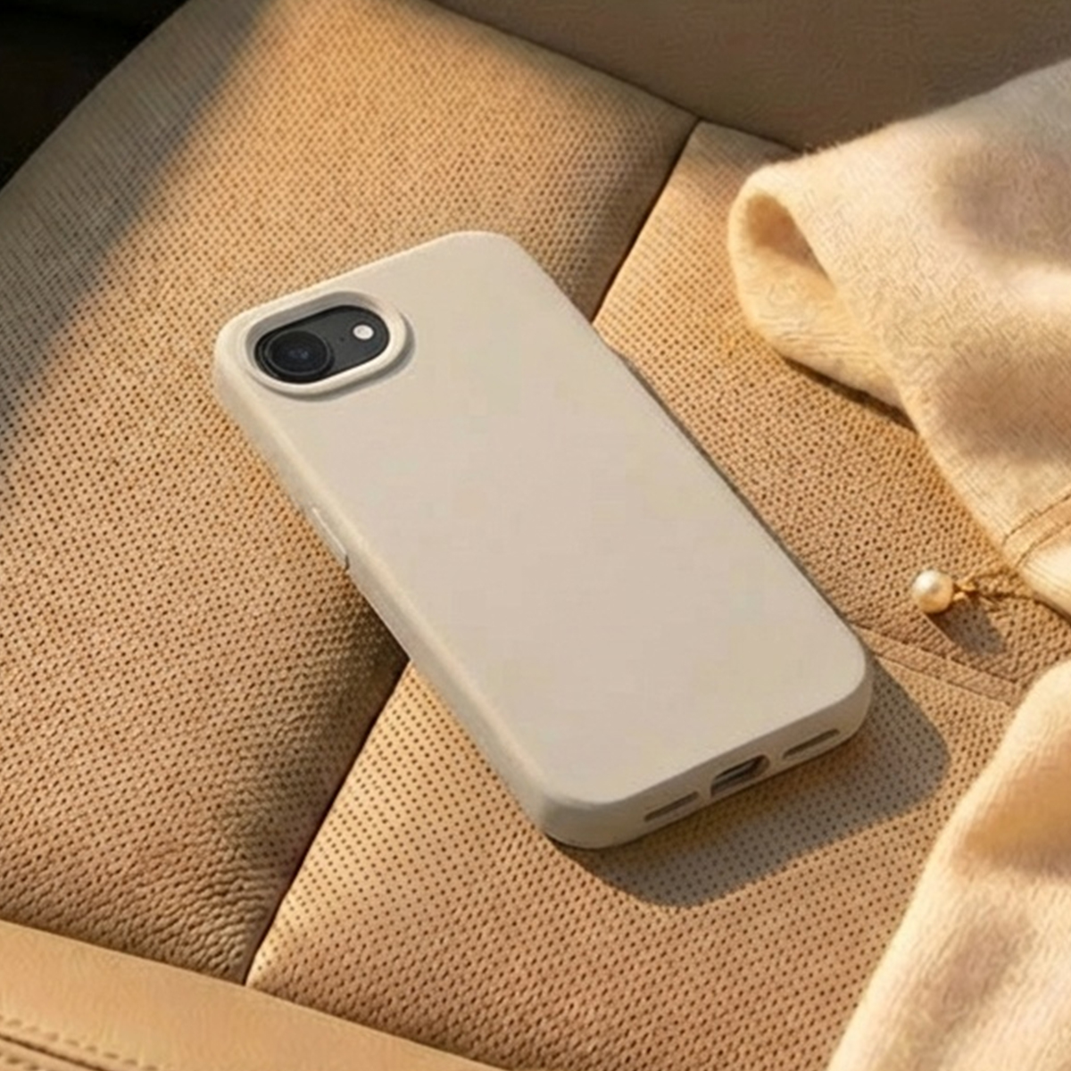 Uno smartphone grigio chiaro giace su un sedile beige con un panno beige accanto.